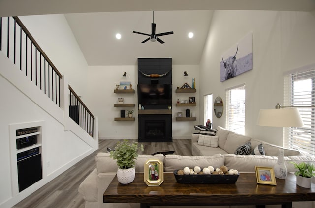 living room with ceiling fan, a towering ceiling, and hardwood / wood-style floors