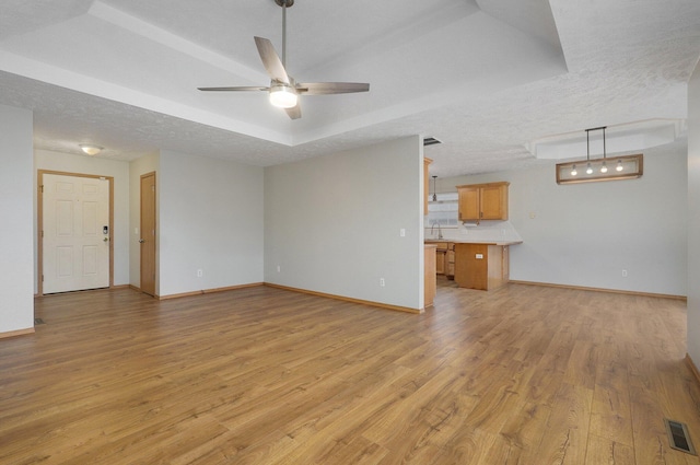 unfurnished living room featuring sink, light hardwood / wood-style flooring, ceiling fan, a textured ceiling, and a raised ceiling