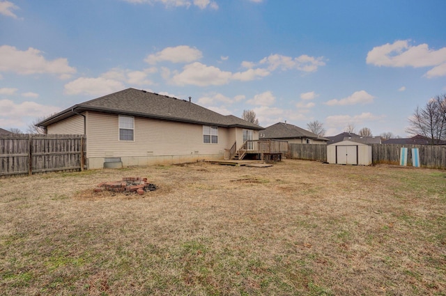 rear view of property featuring a wooden deck, a fire pit, a storage shed, and a lawn