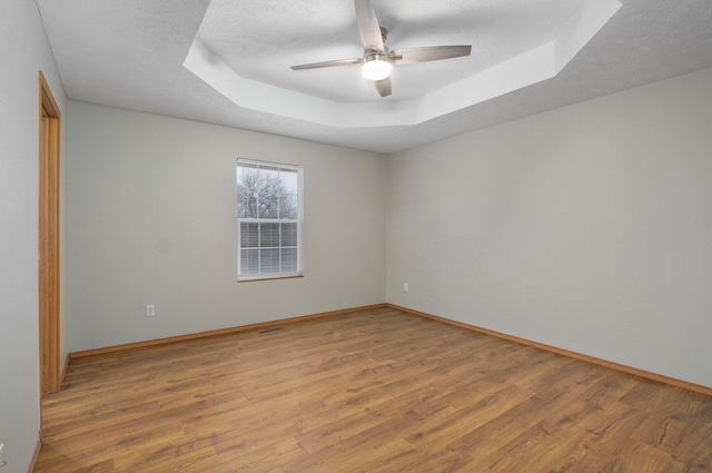 unfurnished room with ceiling fan, a tray ceiling, light hardwood / wood-style flooring, and a textured ceiling