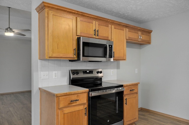 kitchen with appliances with stainless steel finishes, tasteful backsplash, wood-type flooring, ceiling fan, and a textured ceiling