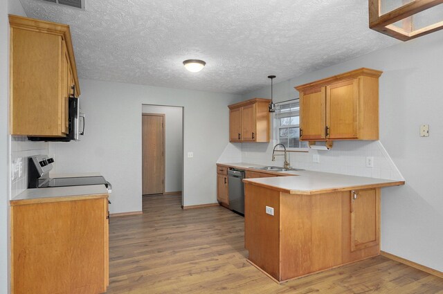 kitchen featuring pendant lighting, sink, appliances with stainless steel finishes, kitchen peninsula, and light wood-type flooring