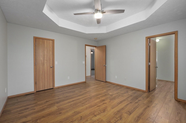 empty room with wood-type flooring, ceiling fan, a textured ceiling, and a tray ceiling