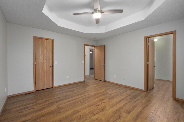 unfurnished room with a raised ceiling, wood-type flooring, ceiling fan, and a textured ceiling