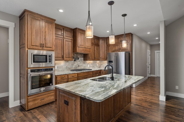 kitchen featuring sink, decorative light fixtures, a center island with sink, appliances with stainless steel finishes, and light stone countertops