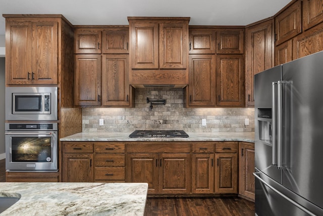 kitchen with tasteful backsplash, dark wood-type flooring, light stone countertops, and appliances with stainless steel finishes