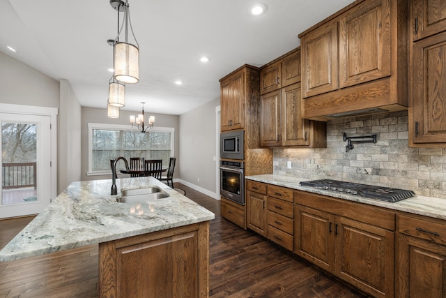 kitchen featuring sink, appliances with stainless steel finishes, light stone countertops, a center island with sink, and decorative light fixtures