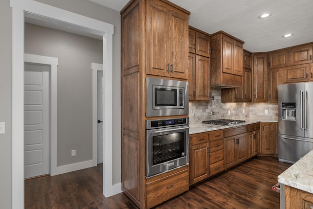 kitchen with tasteful backsplash, appliances with stainless steel finishes, dark hardwood / wood-style flooring, and light stone countertops