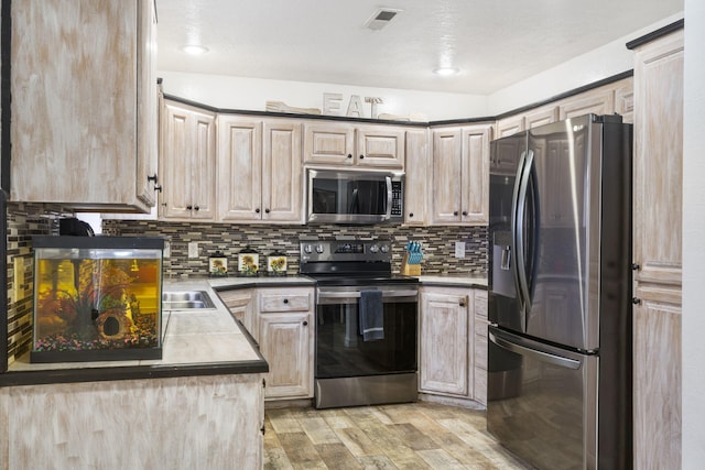 kitchen featuring sink, light wood-type flooring, light brown cabinets, stainless steel appliances, and decorative backsplash