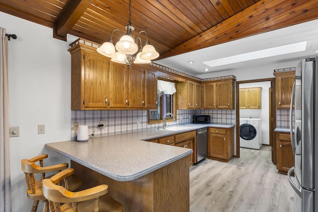 kitchen featuring washer / dryer, decorative light fixtures, kitchen peninsula, stainless steel appliances, and backsplash