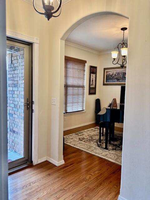 foyer entrance with wood-type flooring, ornamental molding, and a chandelier