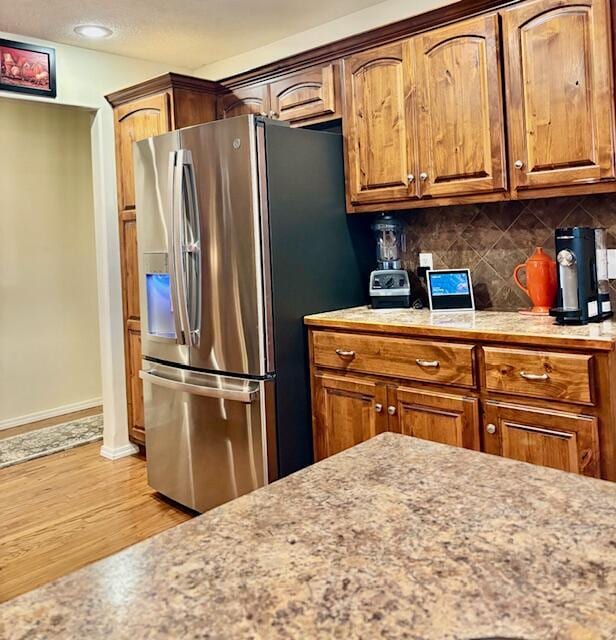 kitchen featuring stainless steel fridge, light hardwood / wood-style floors, and decorative backsplash