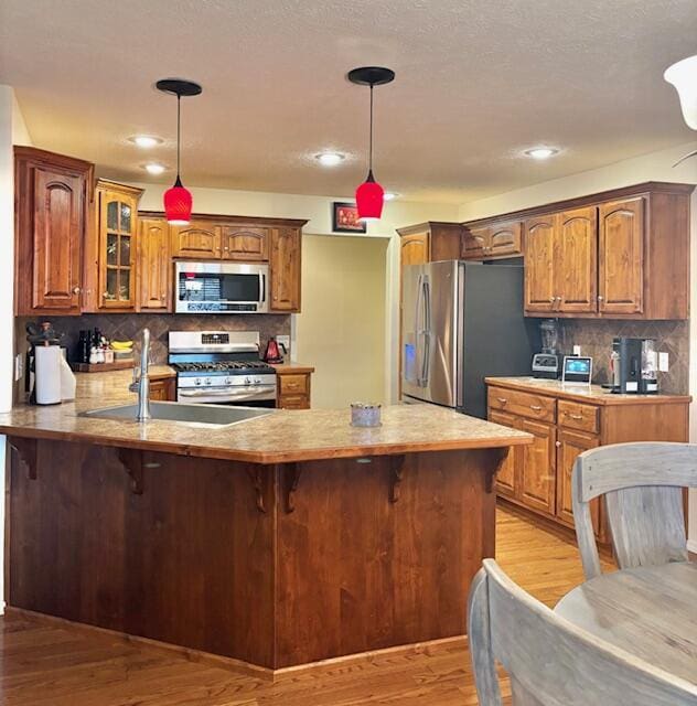 kitchen with appliances with stainless steel finishes, kitchen peninsula, sink, and hanging light fixtures