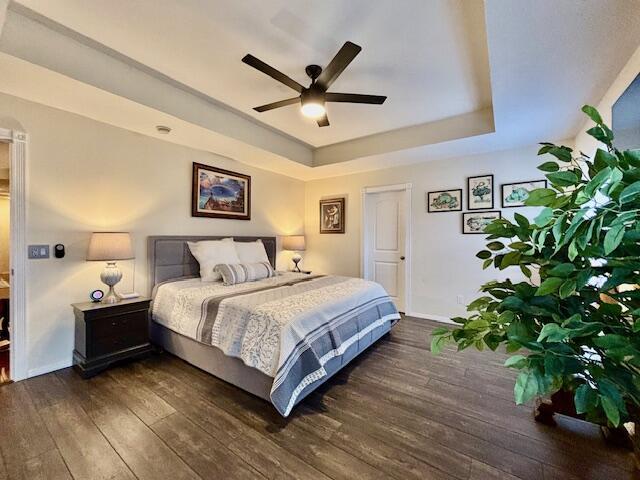 bedroom with dark wood-type flooring, ceiling fan, and a raised ceiling