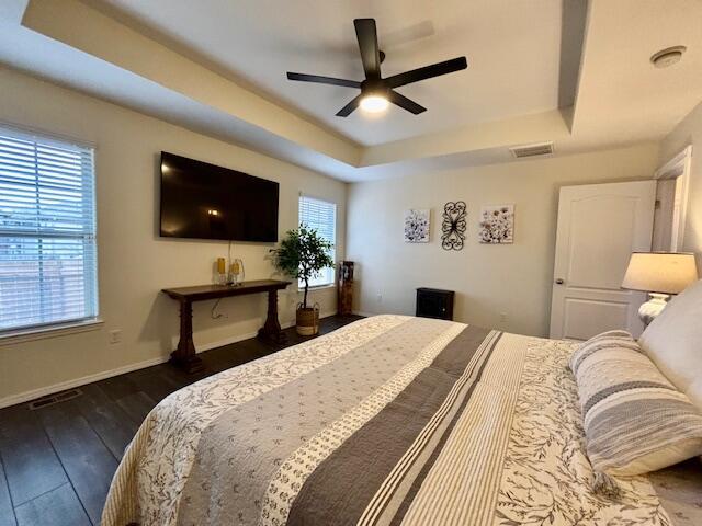 bedroom featuring a raised ceiling, dark hardwood / wood-style floors, and ceiling fan