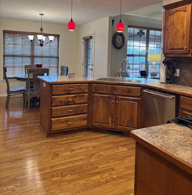 kitchen featuring hanging light fixtures, sink, stainless steel dishwasher, and light hardwood / wood-style flooring