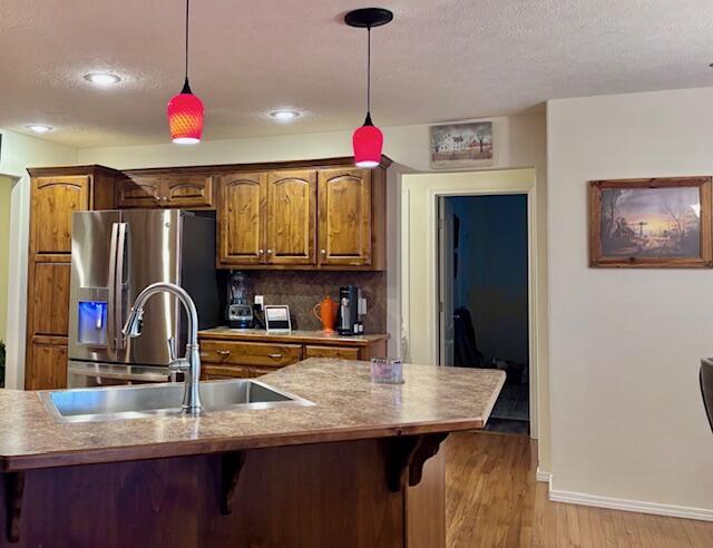 kitchen with tasteful backsplash, sink, hanging light fixtures, stainless steel fridge with ice dispenser, and light wood-type flooring