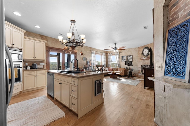 kitchen with cream cabinets, sink, light hardwood / wood-style flooring, stainless steel appliances, and a kitchen island with sink