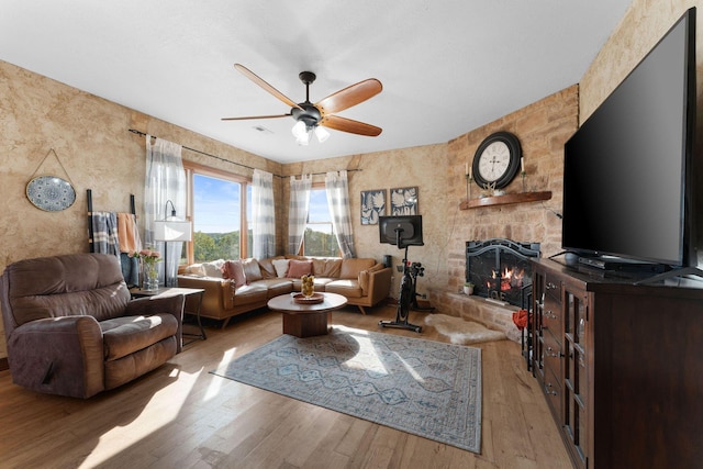 living room featuring ceiling fan, a fireplace, and light hardwood / wood-style flooring