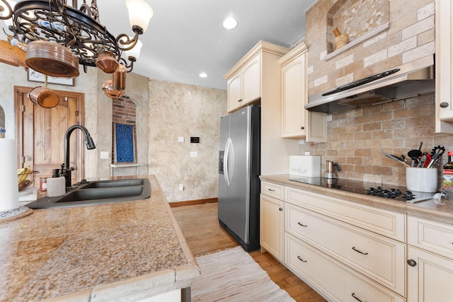 kitchen with sink, stainless steel fridge, black electric stovetop, light hardwood / wood-style floors, and cream cabinets