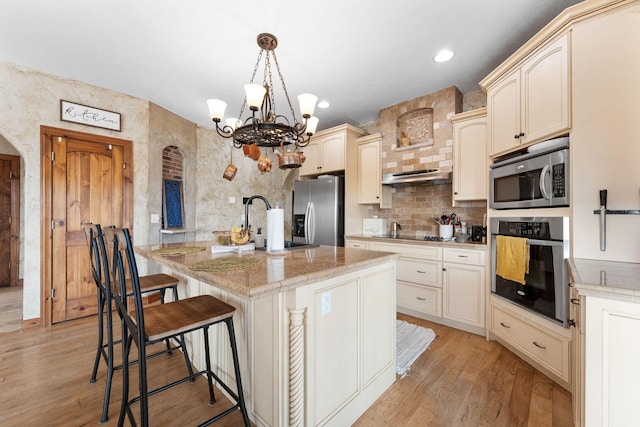 kitchen with appliances with stainless steel finishes, a breakfast bar area, hanging light fixtures, a center island, and light stone countertops