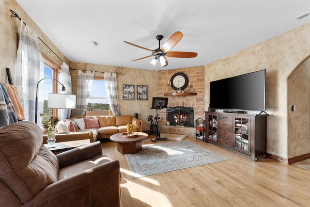 living room featuring ceiling fan, a stone fireplace, and light hardwood / wood-style floors