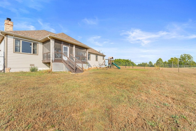 back of house with a playground, a sunroom, and a lawn