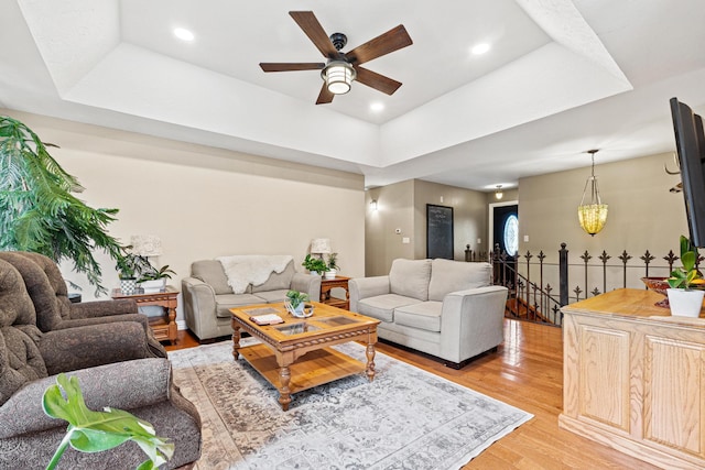 living room with light hardwood / wood-style floors, a raised ceiling, and ceiling fan