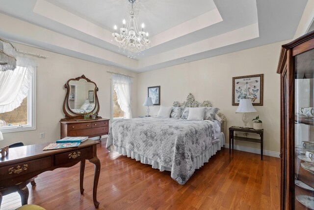 bedroom with a raised ceiling, dark wood-type flooring, and an inviting chandelier