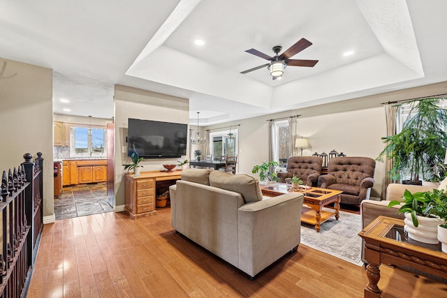 living room with a healthy amount of sunlight, a raised ceiling, and light hardwood / wood-style flooring