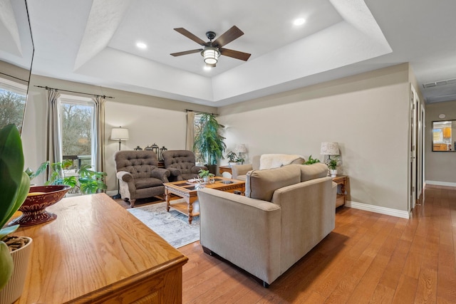 living room featuring ceiling fan, a raised ceiling, and light hardwood / wood-style flooring