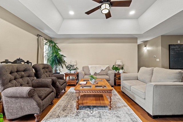 living room featuring a raised ceiling, wood-type flooring, and ceiling fan