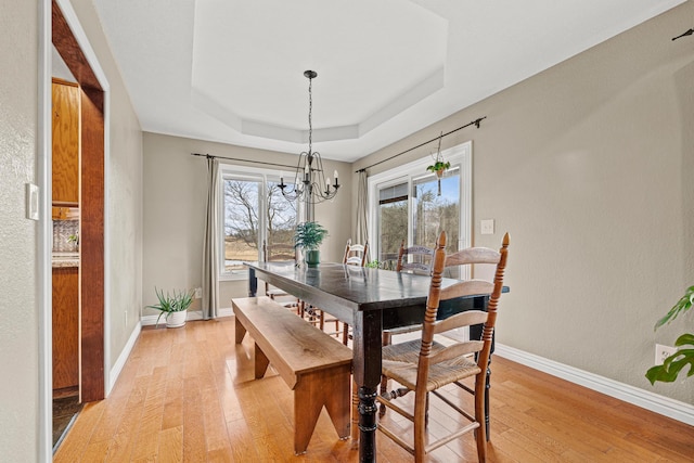 dining room with a raised ceiling, a chandelier, and light wood-type flooring