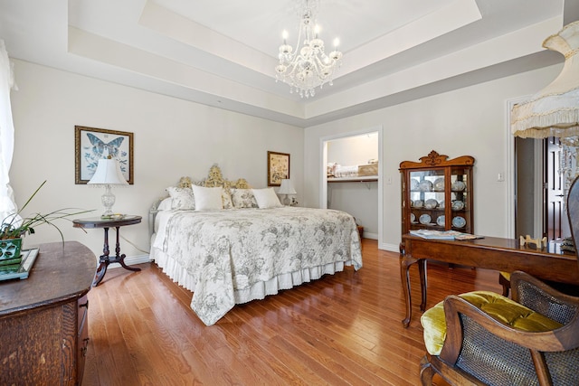 bedroom with wood-type flooring, an inviting chandelier, and a tray ceiling