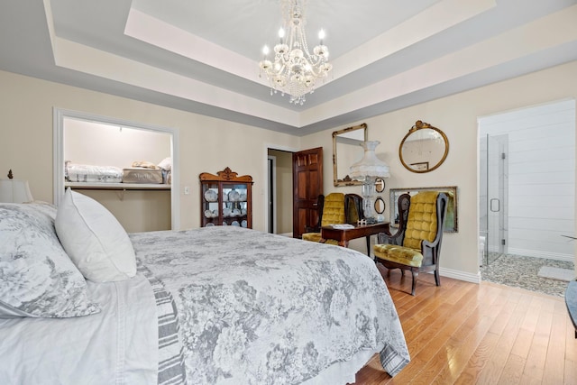 bedroom featuring a raised ceiling, an inviting chandelier, and light wood-type flooring