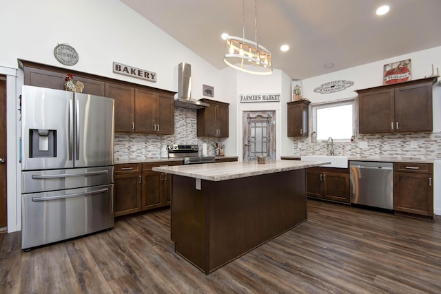 kitchen with appliances with stainless steel finishes, sink, a center island, wall chimney exhaust hood, and hanging light fixtures