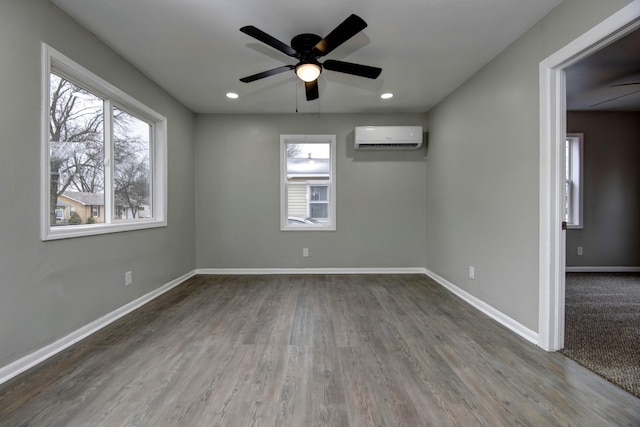 spare room with wood-type flooring, a wall unit AC, and ceiling fan