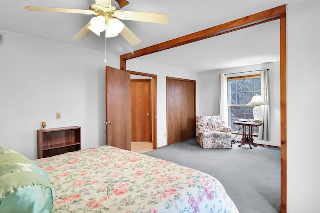 carpeted bedroom with multiple closets, beamed ceiling, and ceiling fan