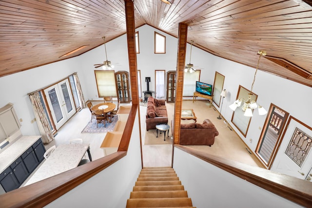 stairs with a wood stove, ceiling fan with notable chandelier, wood ceiling, and high vaulted ceiling