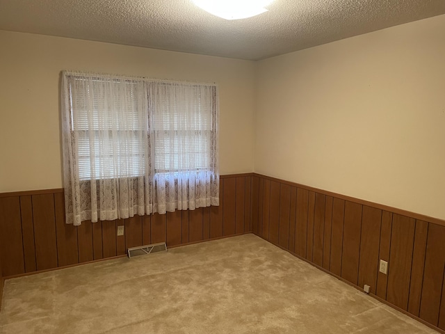 empty room with wooden walls, light colored carpet, and a textured ceiling