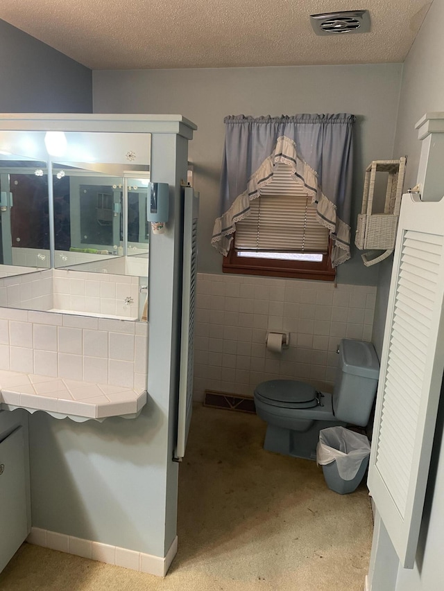 bathroom with tile walls, toilet, and a textured ceiling