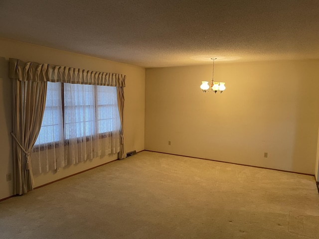 carpeted spare room with a textured ceiling and a chandelier