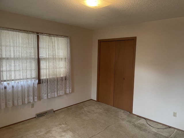 unfurnished bedroom featuring light carpet, a textured ceiling, and a closet