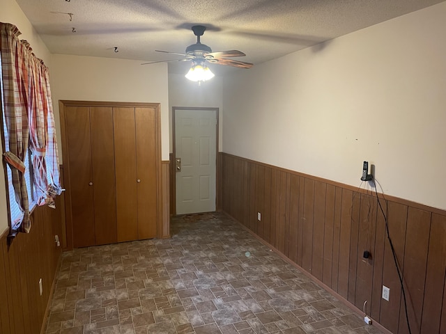 empty room featuring ceiling fan, wooden walls, and a textured ceiling