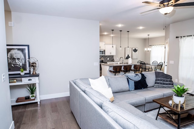 living room with sink, ceiling fan with notable chandelier, and dark wood-type flooring