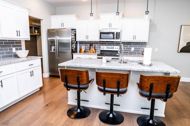 kitchen with a kitchen island with sink, hanging light fixtures, stainless steel appliances, and a kitchen breakfast bar