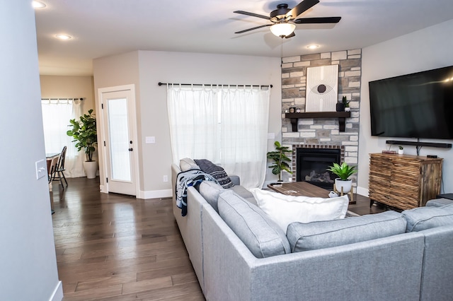 living room featuring ceiling fan, dark hardwood / wood-style floors, and a stone fireplace