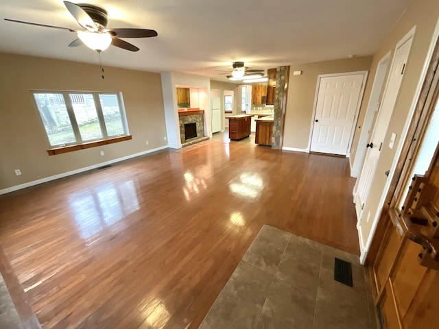 unfurnished living room featuring hardwood / wood-style flooring, a stone fireplace, and ceiling fan