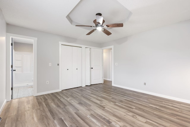 unfurnished bedroom with multiple closets, ensuite bath, ceiling fan, and light hardwood / wood-style floors