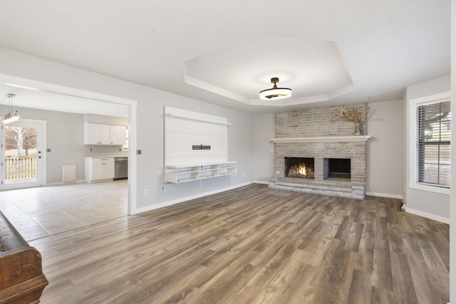 unfurnished living room with a raised ceiling, a textured ceiling, a fireplace, and light hardwood / wood-style flooring